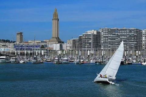 Voilier dans la baie devant une marina de mâts et la ville.