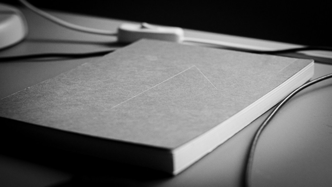 Carnet fermé en gros plan sur bureau minimaliste noir et blanc, pages blanches visibles.