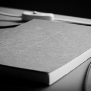 Carnet fermé en gros plan sur bureau minimaliste noir et blanc, pages blanches visibles.