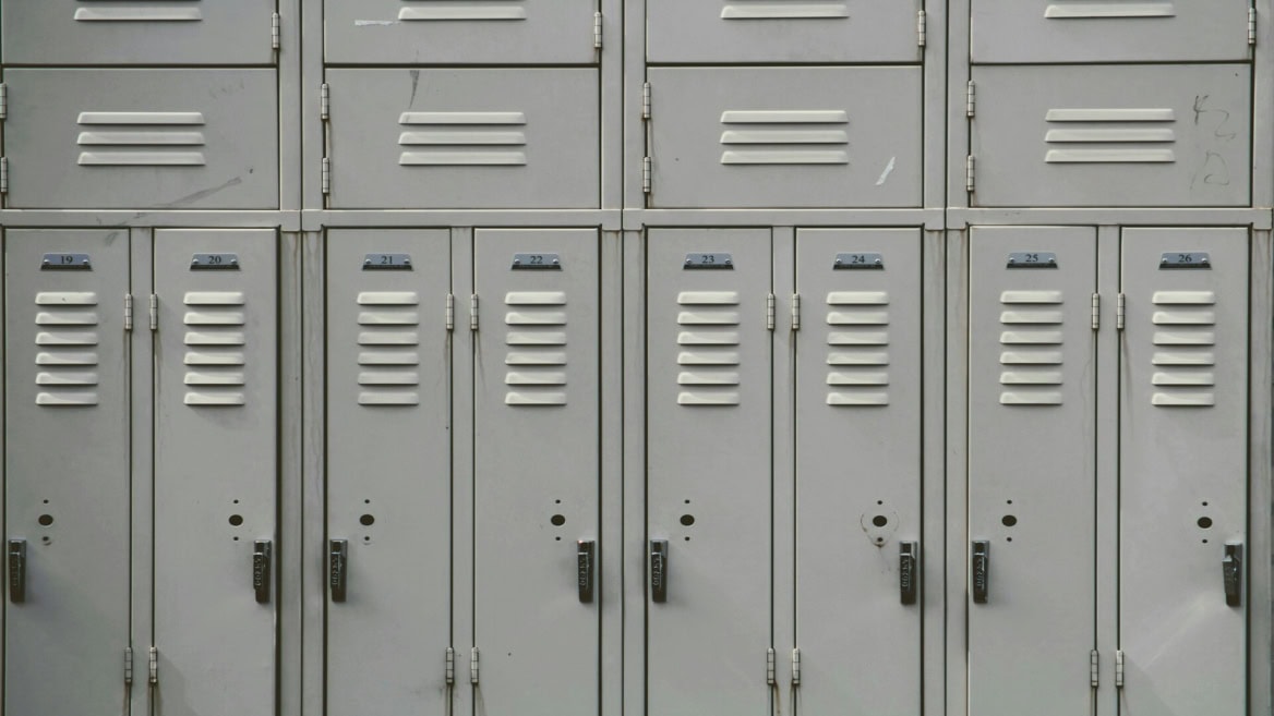 Casiers métalliques numérotés 19 à 26 dans un vestiaire scolaire, serrures visibles.