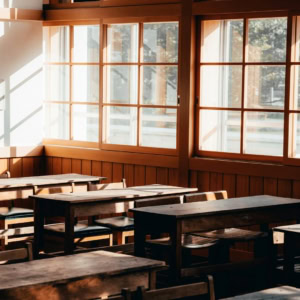 Classe vintage vide baignée de lumière naturelle, bureaux en bois et grandes fenêtres à carreaux.