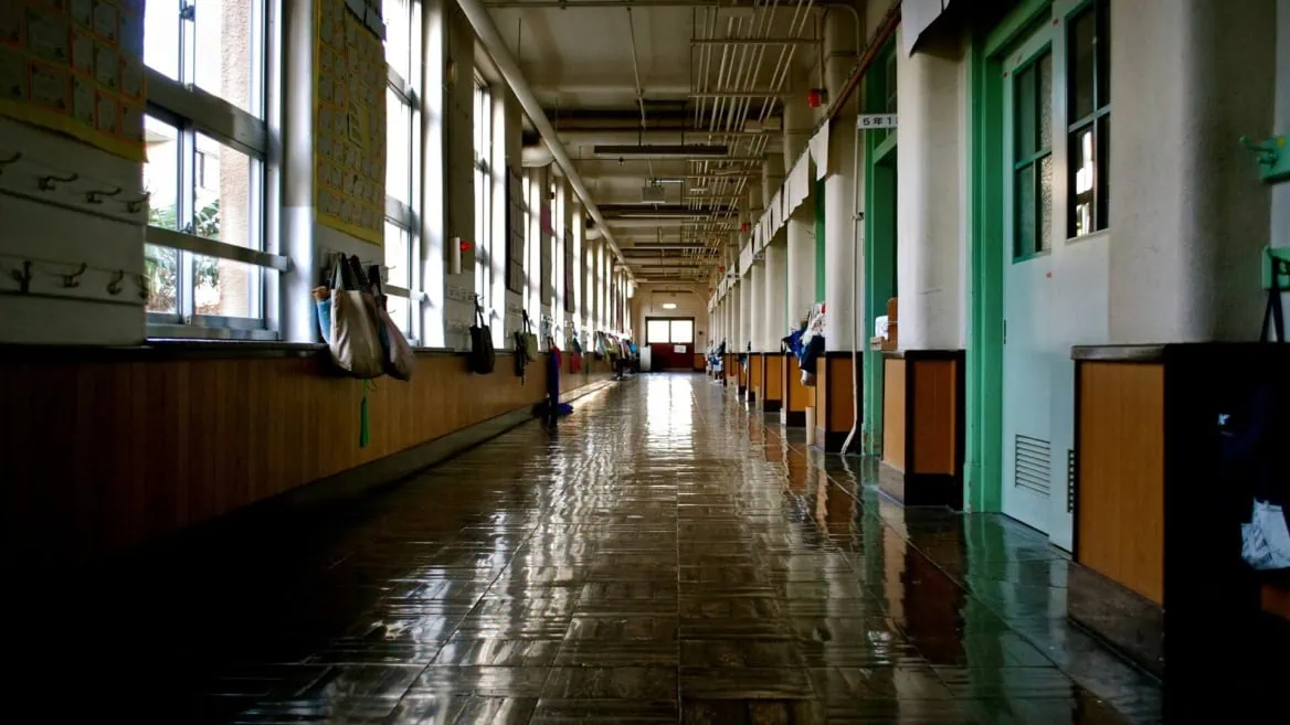 Couloir scolaire vide en perspective, sol brillant reflétant fenêtres, portes et sacs délèves.