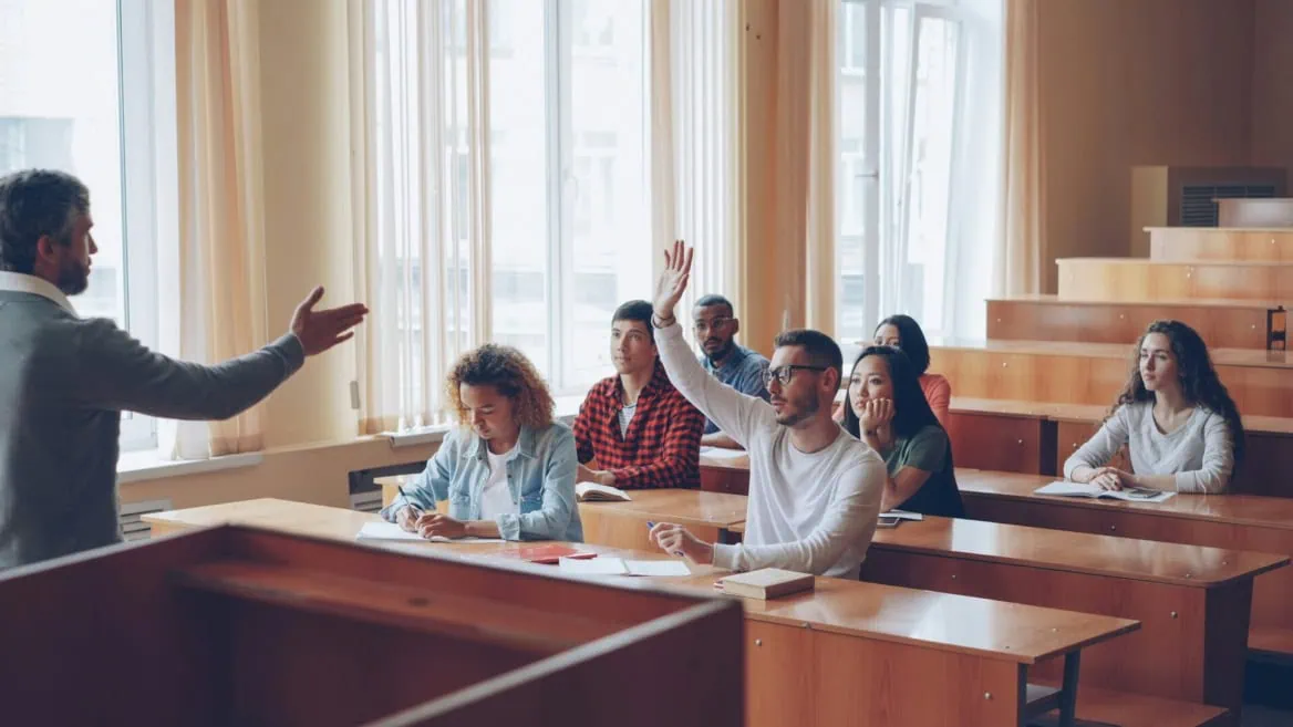 Cours universitaire en amphithéâtre, professeur interactif, étudiant lève la main et prise de notes.