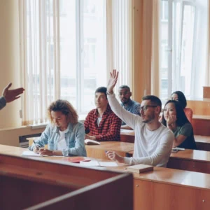 Cours universitaire en amphithéâtre, professeur interactif, étudiant lève la main et prise de notes.