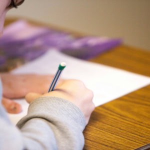 Personne concentrée, main écrivant au stylo rayé sur papier posé sur bureau en bois.