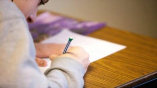 Personne concentrée, main écrivant au stylo rayé sur papier posé sur bureau en bois.