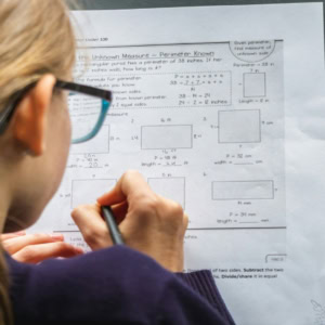 Élève écrivant des exercices de périmètre et mesures sur feuille de mathématiques avec crayon.