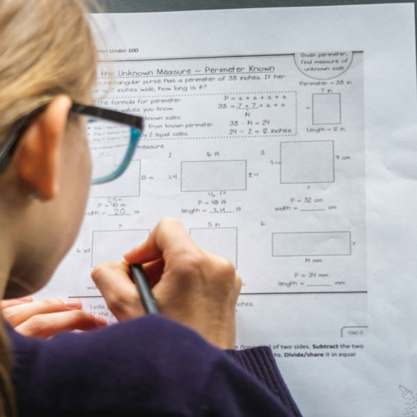 Élève écrivant des exercices de périmètre et mesures sur feuille de mathématiques avec crayon.