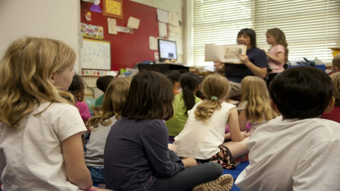 Enfants décole élémentaire écoutant une lecture en classe, enseignant tenant un livre.