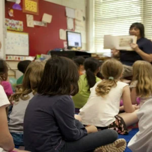 Enfants décole élémentaire écoutant une lecture en classe, enseignant tenant un livre.