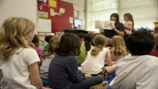Enfants décole élémentaire écoutant une lecture en classe, enseignant tenant un livre.