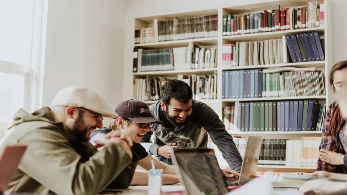Étudiants en groupe souriants au travail collaboratif sur ordinateurs en bibliothèque.