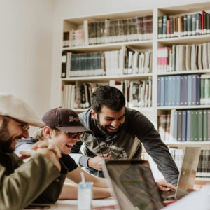 Étudiants en groupe souriants au travail collaboratif sur ordinateurs en bibliothèque.