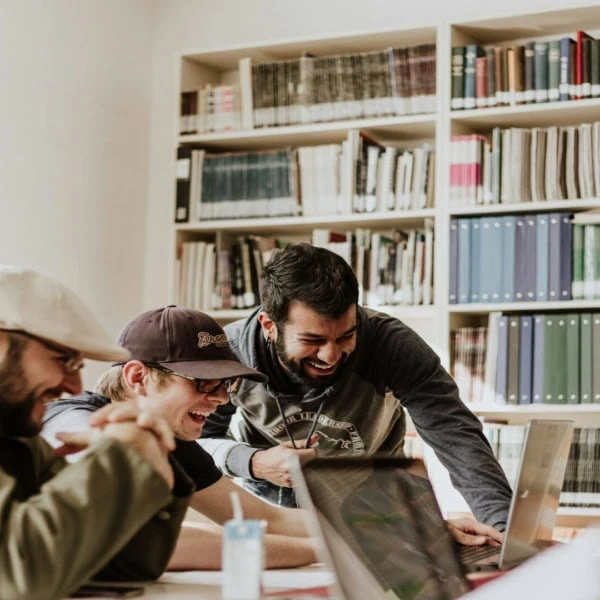 Étudiants en groupe souriants au travail collaboratif sur ordinateurs en bibliothèque.