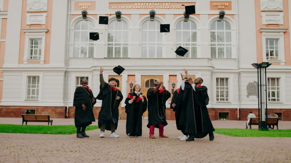 Étudiants diplômés lançant leurs toques sur le campus devant bâtiment académique.