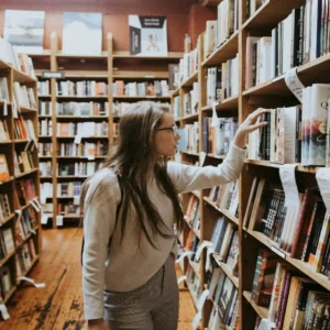 Librairie indépendante, allée de rayonnages en bois, personne feuilletant des livres.