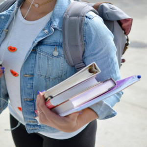 Étudiant(e) marchant avec livres, veste en jean, sac à dos et dossier violet.