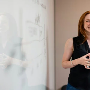 Femme rousse souriante devant tableau blanc en réunion de brainstorming au bureau.