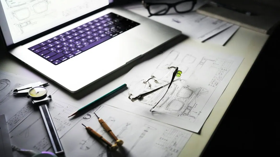 Poste de travail lunettes et dessins techniques avec pied à coulisse et ordinateur portable.