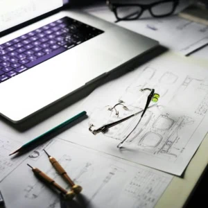 Poste de travail lunettes et dessins techniques avec pied à coulisse et ordinateur portable.