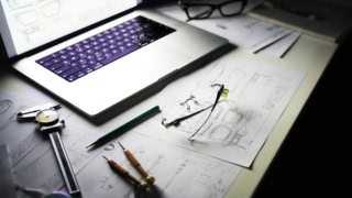 Poste de travail lunettes et dessins techniques avec pied à coulisse et ordinateur portable.