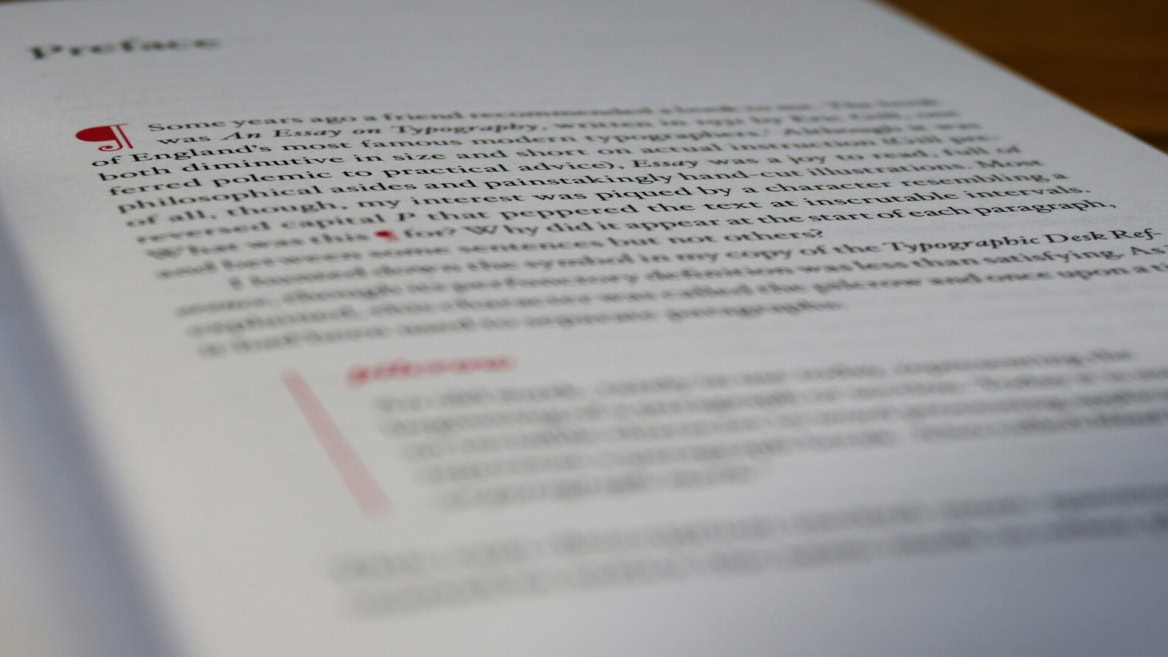 Gros plan dune page de préface typographique avec lettrine rouge, papier texturé, faible profondeur de champ.