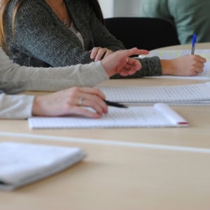 Prise de notes en réunion collaborative : mains, stylos et cahiers sur table.