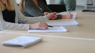 Prise de notes en réunion collaborative : mains, stylos et cahiers sur table.