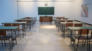 Salle de classe vide symétrique avec rangées de pupitres, bureau du professeur et tableau noir.