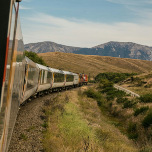 Train sinueux en campagne traversant collines et montagnes, locomotive rouge sur voie ferrée.