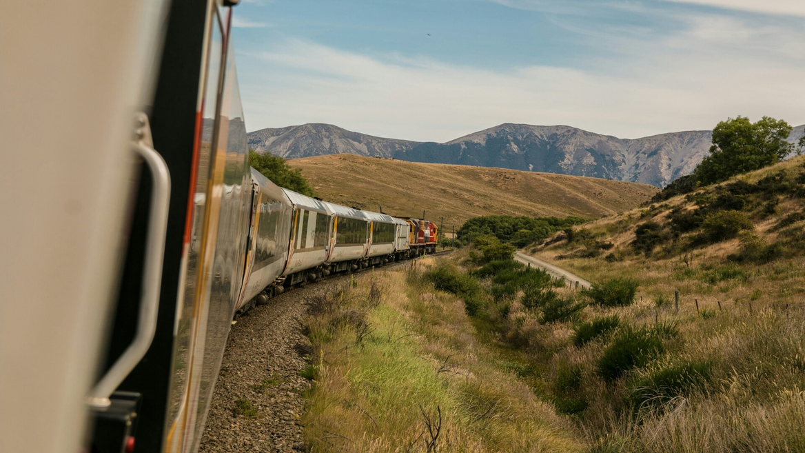 Train sinueux en campagne traversant collines et montagnes, locomotive rouge sur voie ferrée.