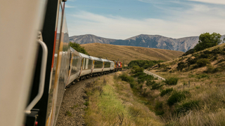 Train sinueux en campagne traversant collines et montagnes, locomotive rouge sur voie ferrée.