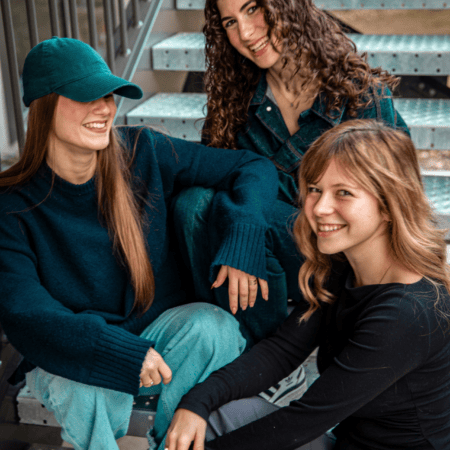 Trois amies souriantes sur un escalier métallique industriel, portrait mode décontracté.