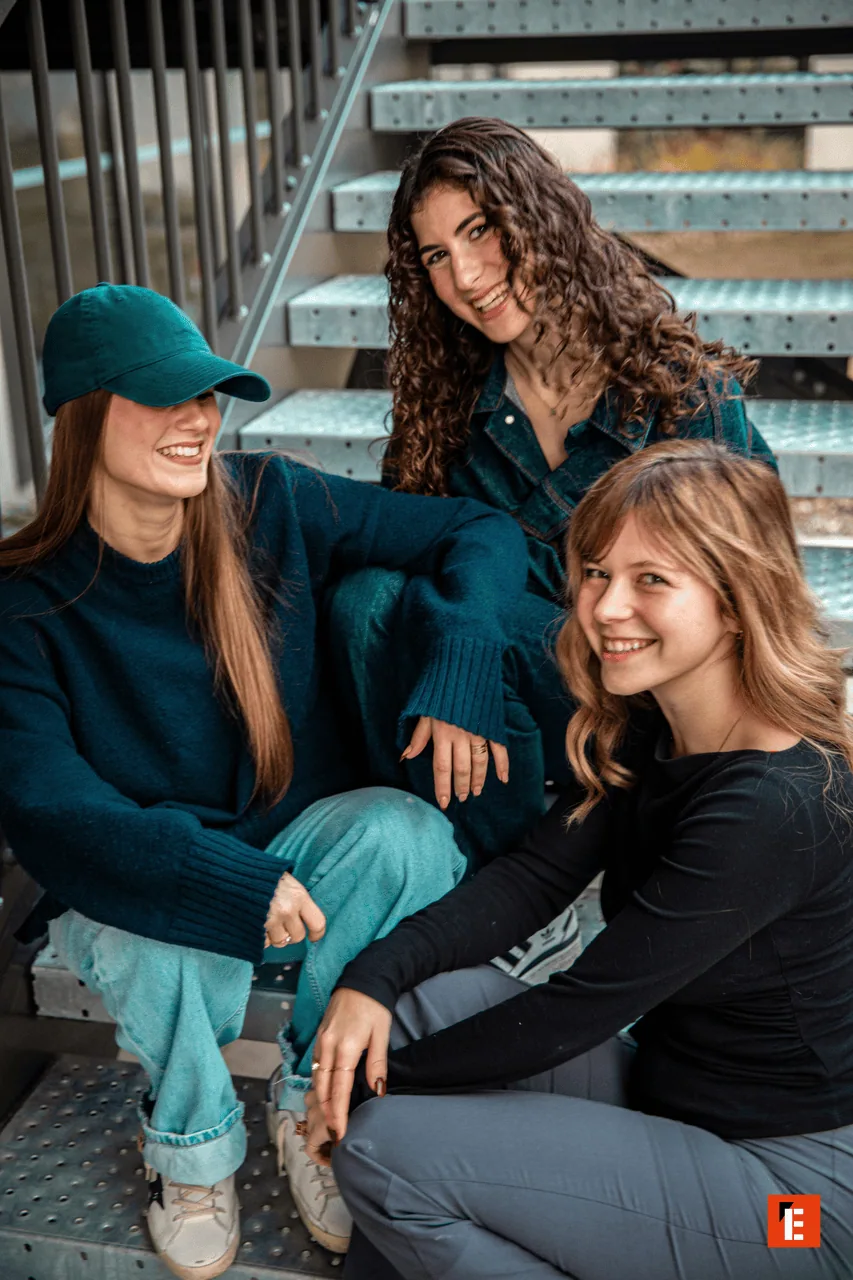 Trois amies souriantes sur un escalier métallique industriel, portrait mode décontracté.