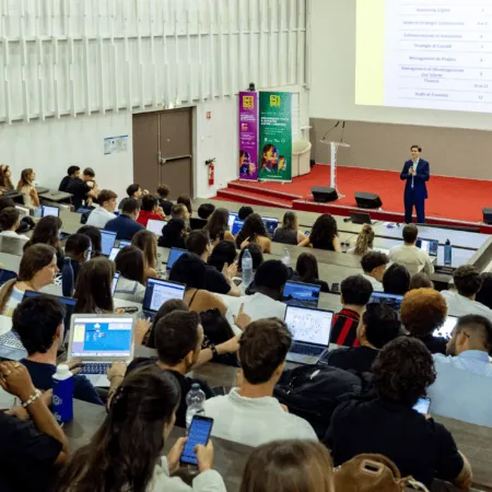 Amphithéâtre universitaire plein détudiants lors dune présentation avec ordinateurs portables.
