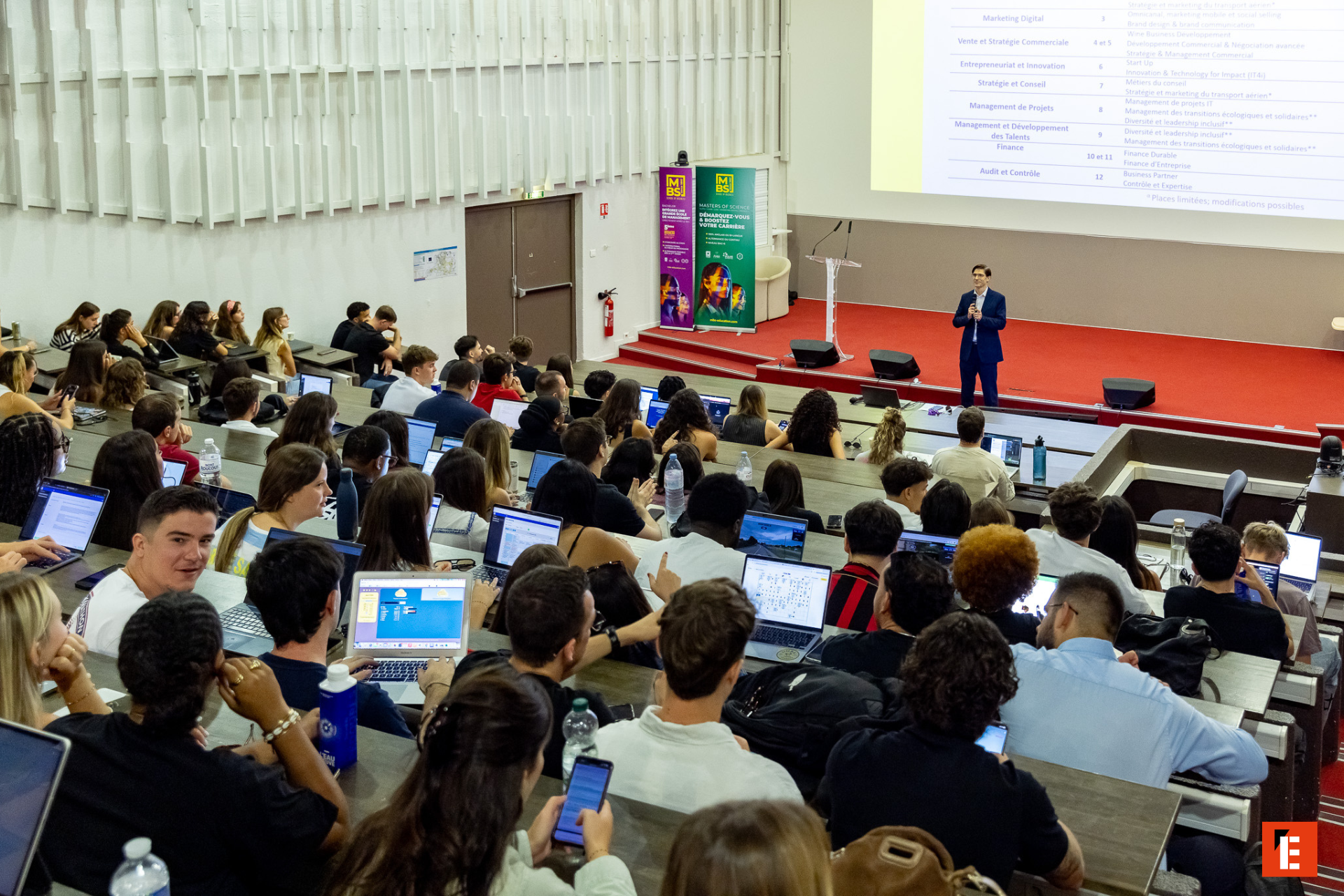 Amphithéâtre universitaire plein détudiants lors dune présentation avec ordinateurs portables.
