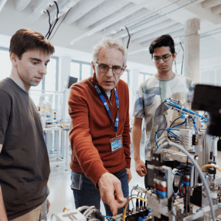 Atelier dautomatisation : ingénieur expliquant prototype industriel avec capteurs, câbles et actionneurs.