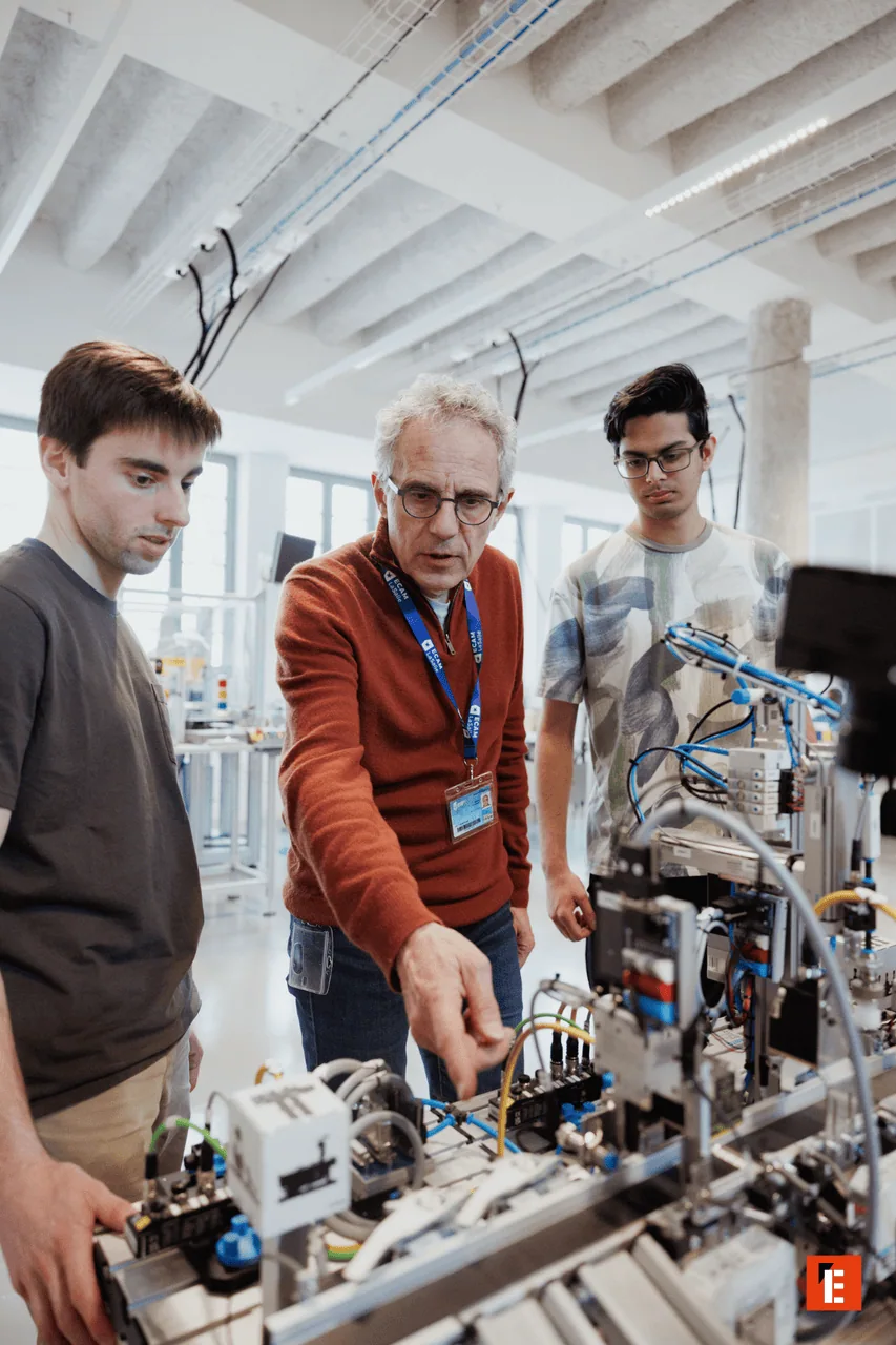 Atelier dautomatisation : ingénieur expliquant prototype industriel avec capteurs, câbles et actionneurs.