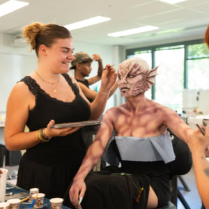 Atelier de maquillage de créature: maquilleurs appliquent prothèse silicone et peinture deffets spéciaux en studio.