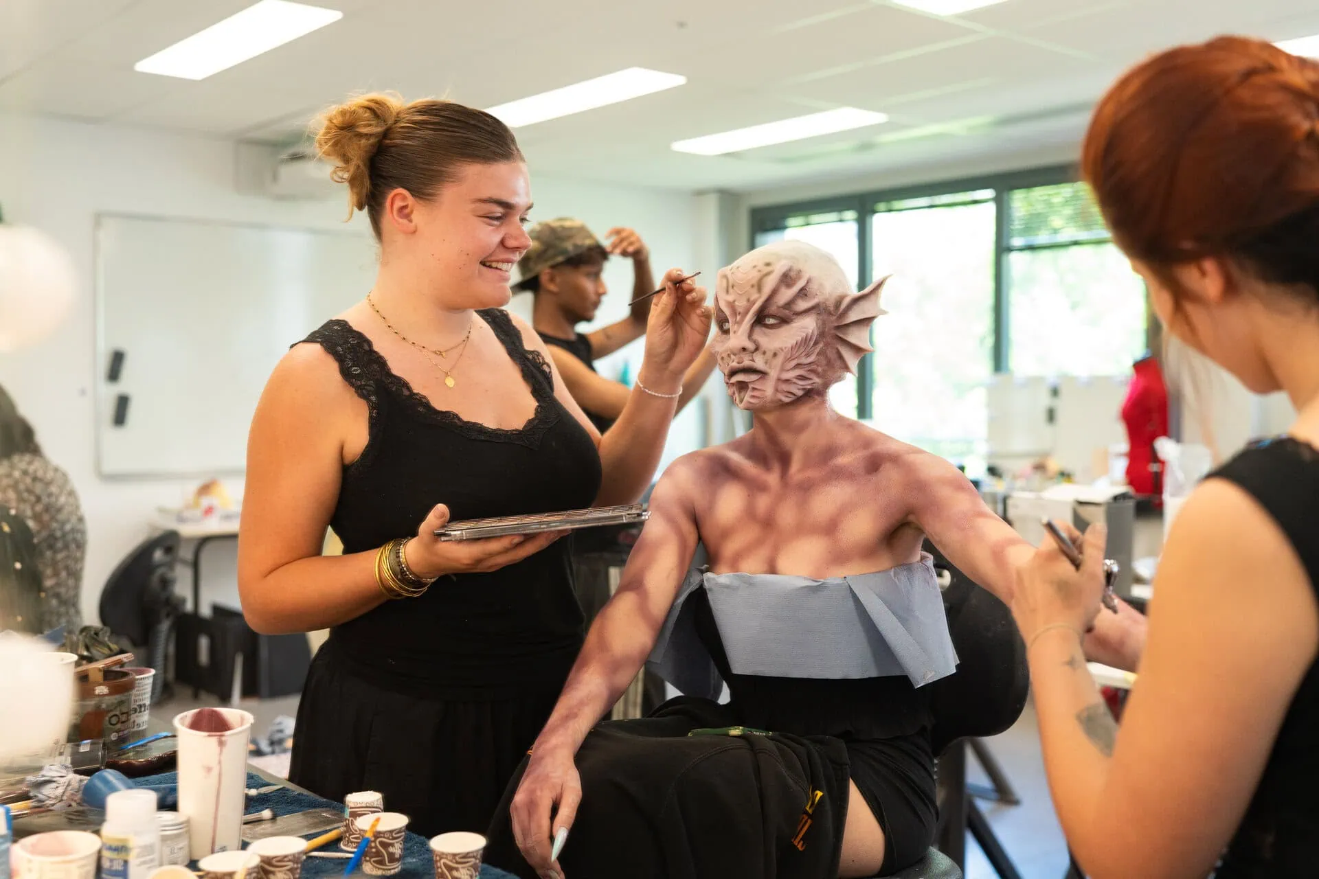 Atelier de maquillage de créature: maquilleurs appliquent prothèse silicone et peinture deffets spéciaux en studio.