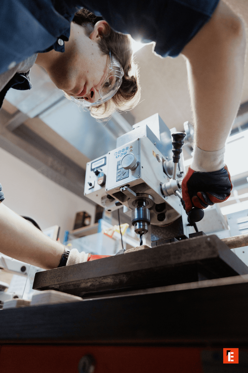 Opérateur en atelier perçage de précision à la perceuse, gants et lunettes de sécurité.