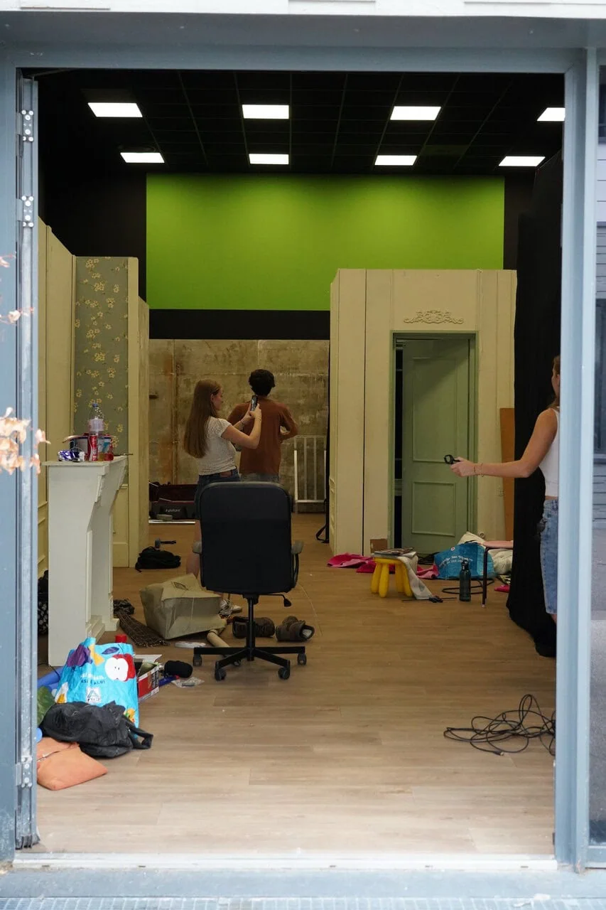 Atelier en travaux, mur vert, chaise à roulettes, plafond lumineux et personnes en action.