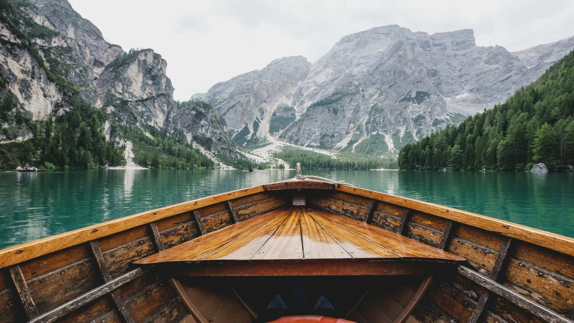 Barque en bois sur lac turquoise, montagnes rocheuses et forêt de conifères en arrière-plan.