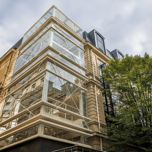 Bâtiment coin contemporain en verre et pierre, escalier vitré moderne contre façade historique.