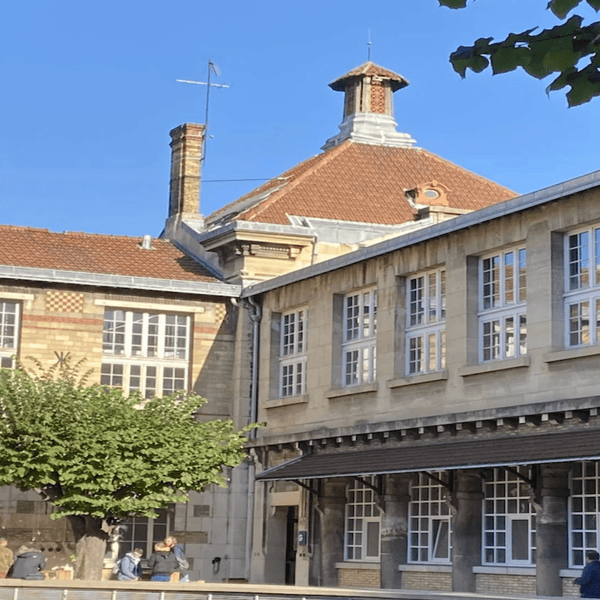 Cour intérieure dun bâtiment historique en pierre et brique, toit en tuiles, arbres et bancs.