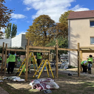 Bénévoles construisent une pergola en bois dans une cour urbaine en automne.
