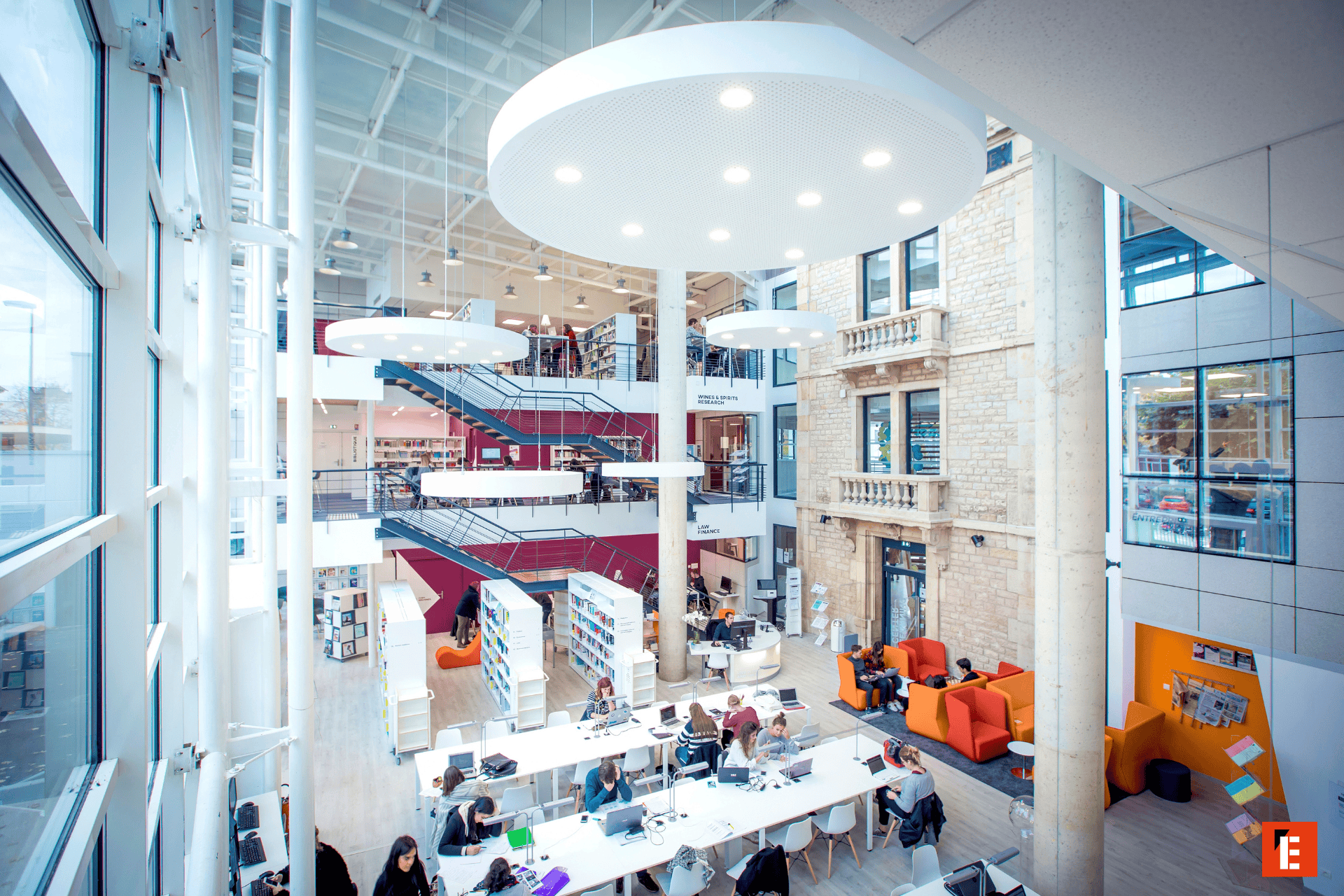 Bibliothèque moderne en atrium lumineux avec étages, escaliers, espaces détude et étudiants.