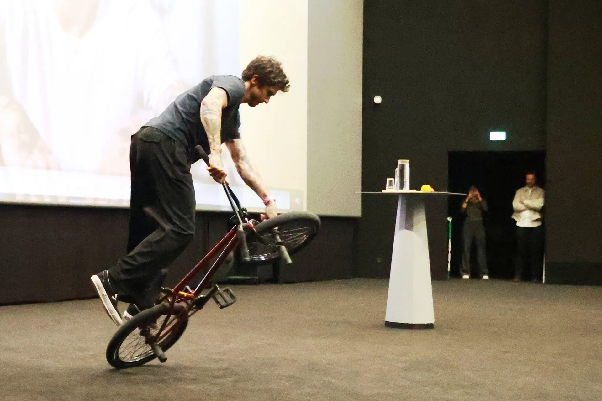 Cycliste BMX exécutant une figure acrobatique en intérieur devant public dans un auditorium.