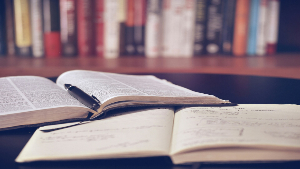 Carnet et stylo sur livre ouvert, table détude près dune bibliothèque.