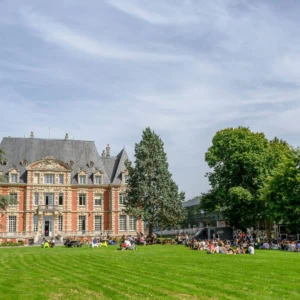 Campus avec pelouse et bâtiment historique en brique, étudiants pique-niquant au soleil.